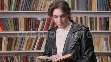 年轻的帅哥穿着黑色皮夹克在图书馆看书，微笑着，正在学习的男学生的画像